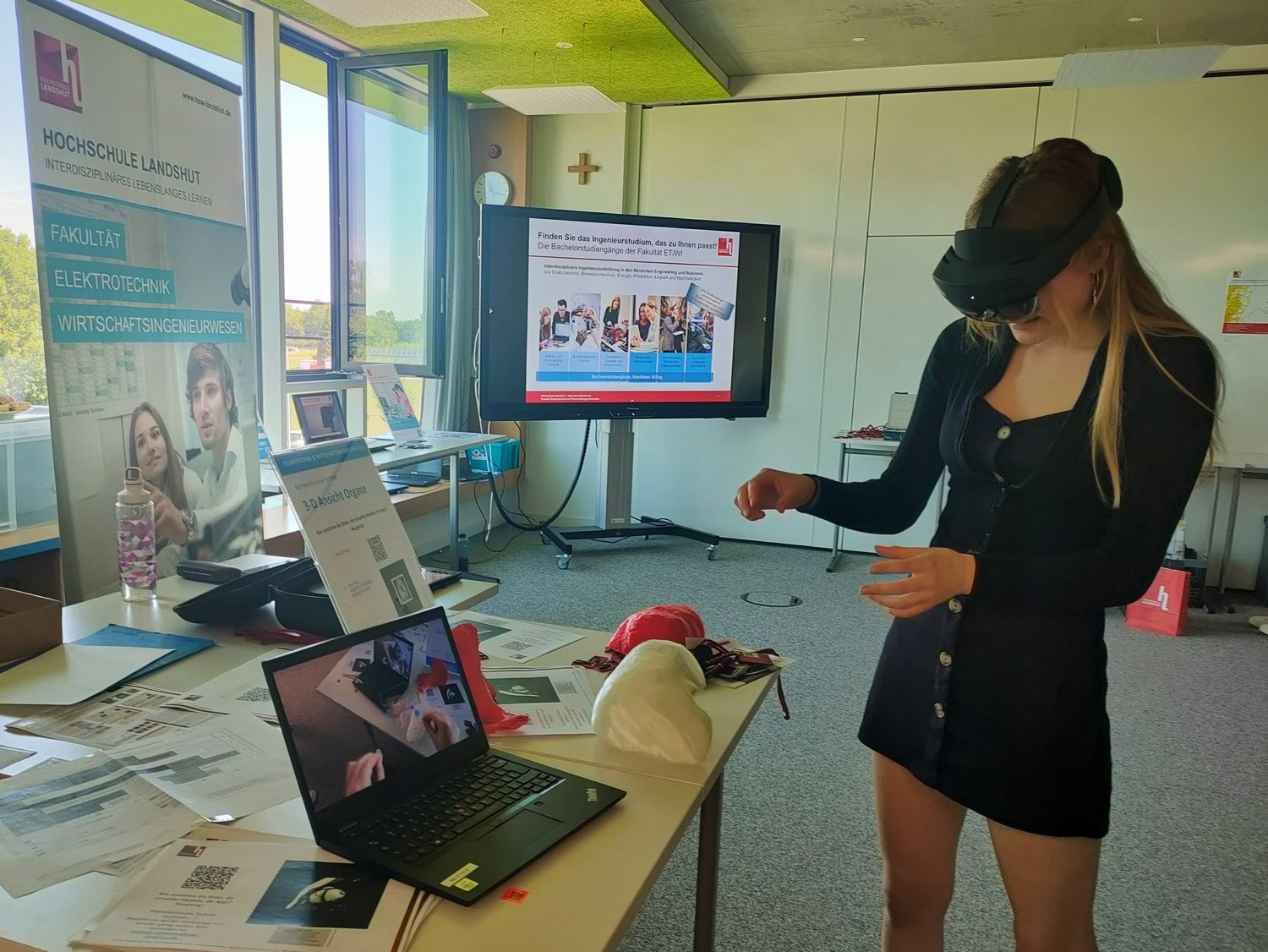 Schülerin mit VR-Brille testet Anwendung im Bereich biomedizinische Technik. Im Hintergrund Monitor, Roll up und Exponate. 