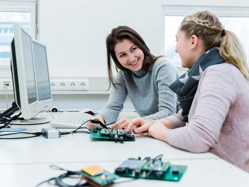 Zwei Studierende sitzen an einem PC-Arbeitsplatz mit Entwicklungsboards für die Programmierung von Mikrocomputern.