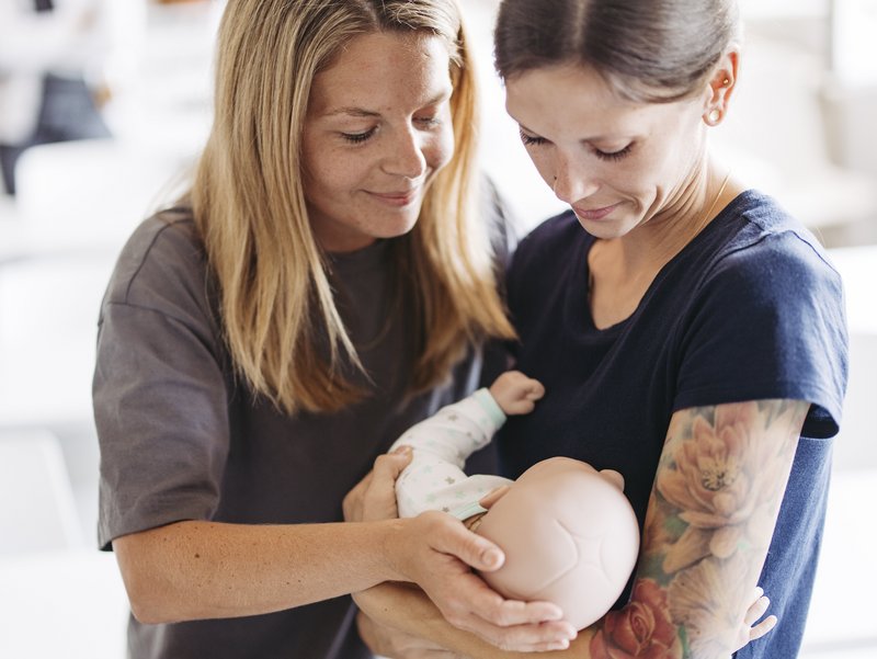 Zwei Frauen halten eine Babypuppe im Arm.