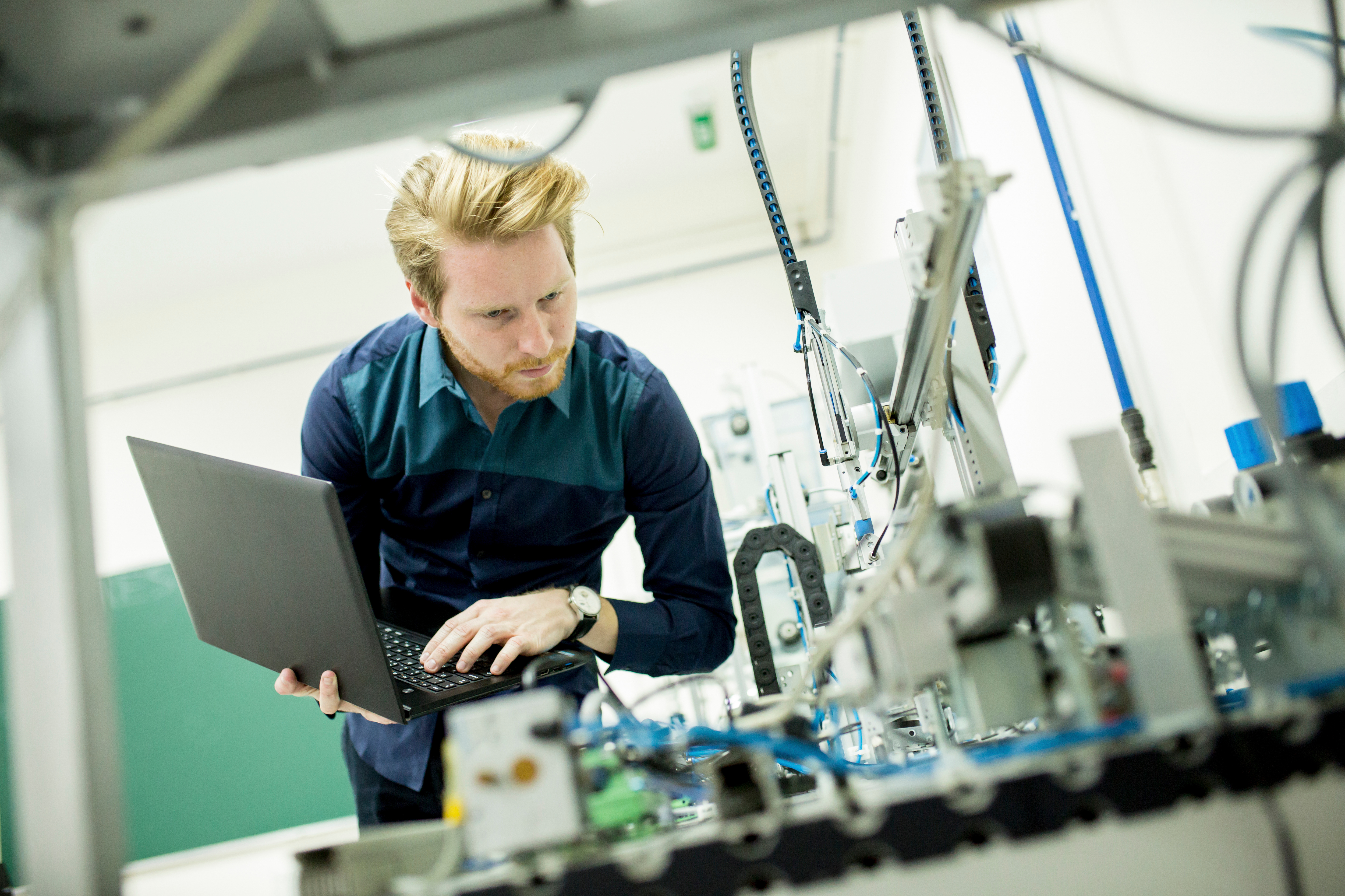 Eine Person mit Laptop bedient einen Produktionstechnik-Aufbau.