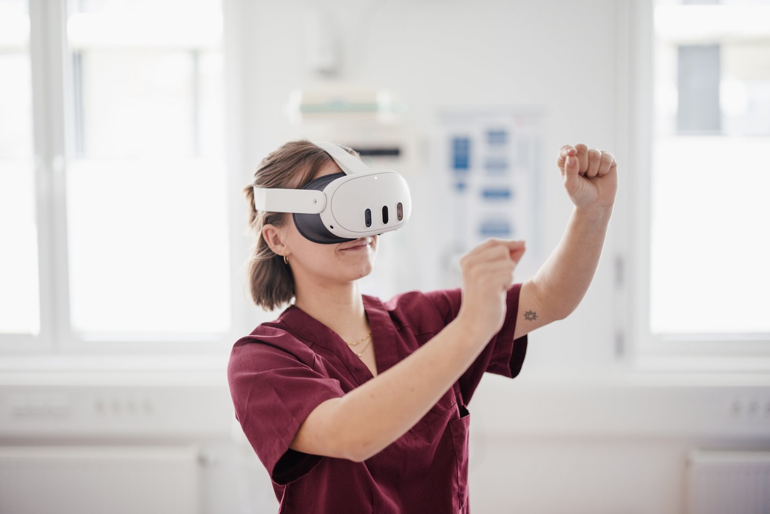 Eine Person trägt eine VR-Brille und interagiert mit einer virtuellen Umgebung. Sie ist in einem medizinischen Umfeld gekleidet und zeigt eine engagierte Körperhaltung, während sie mit den Händen Bewegungen ausführt.
