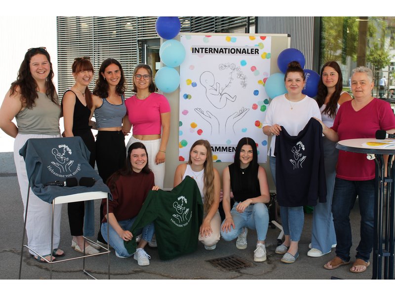 Man sieht die Hebammen-Studierenden gemeinsam mit ihrer Dozentin vor dem Infostand.