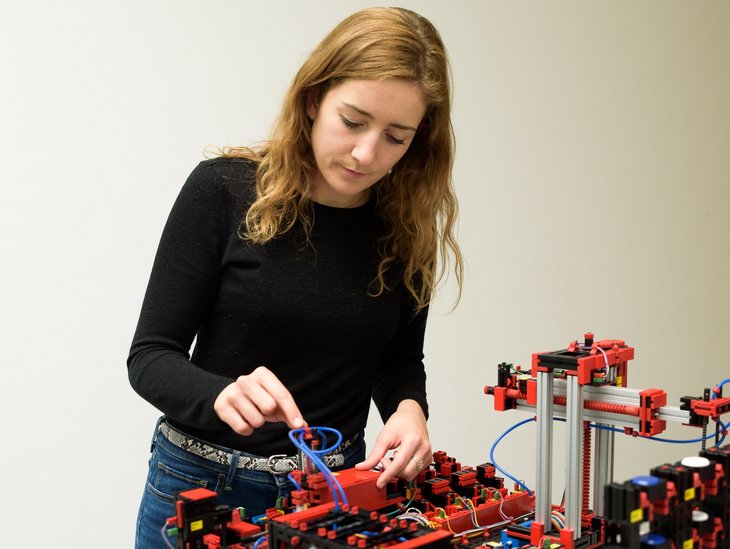 Eine junge Frau steht interessiert vor einem Demonstrationsaufbau für Industrie 4.0. 