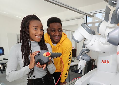 Zwei Personen stehen vor einem Roboter. Eine person hat ein Bedienfeld in der Hand.