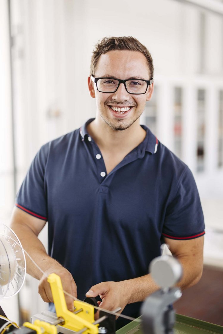 Freundlich zum Betrachter lächelnder Studierender an einem Laborextruder für Kunststoff