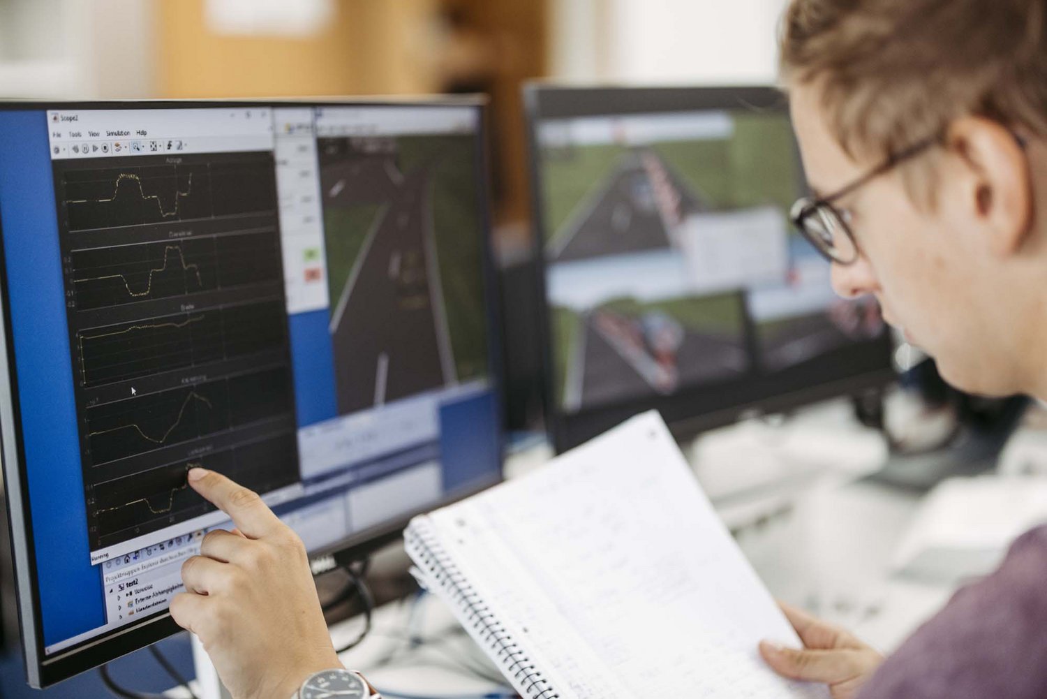 Eine Person sitzt vor einem Computer und hat ein Blatt Papier in ihrer Hand.