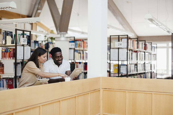 Zwei Personen erklären sich was an einem Stehplatz in der Bibliothek.
