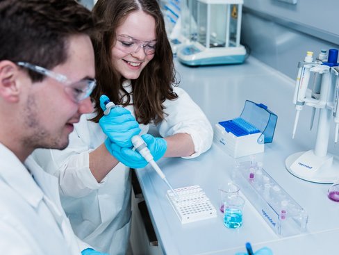 Zwei Studierende sitzen in einem chemischen Labor. Eine Studierende benutzt eine Pipette.