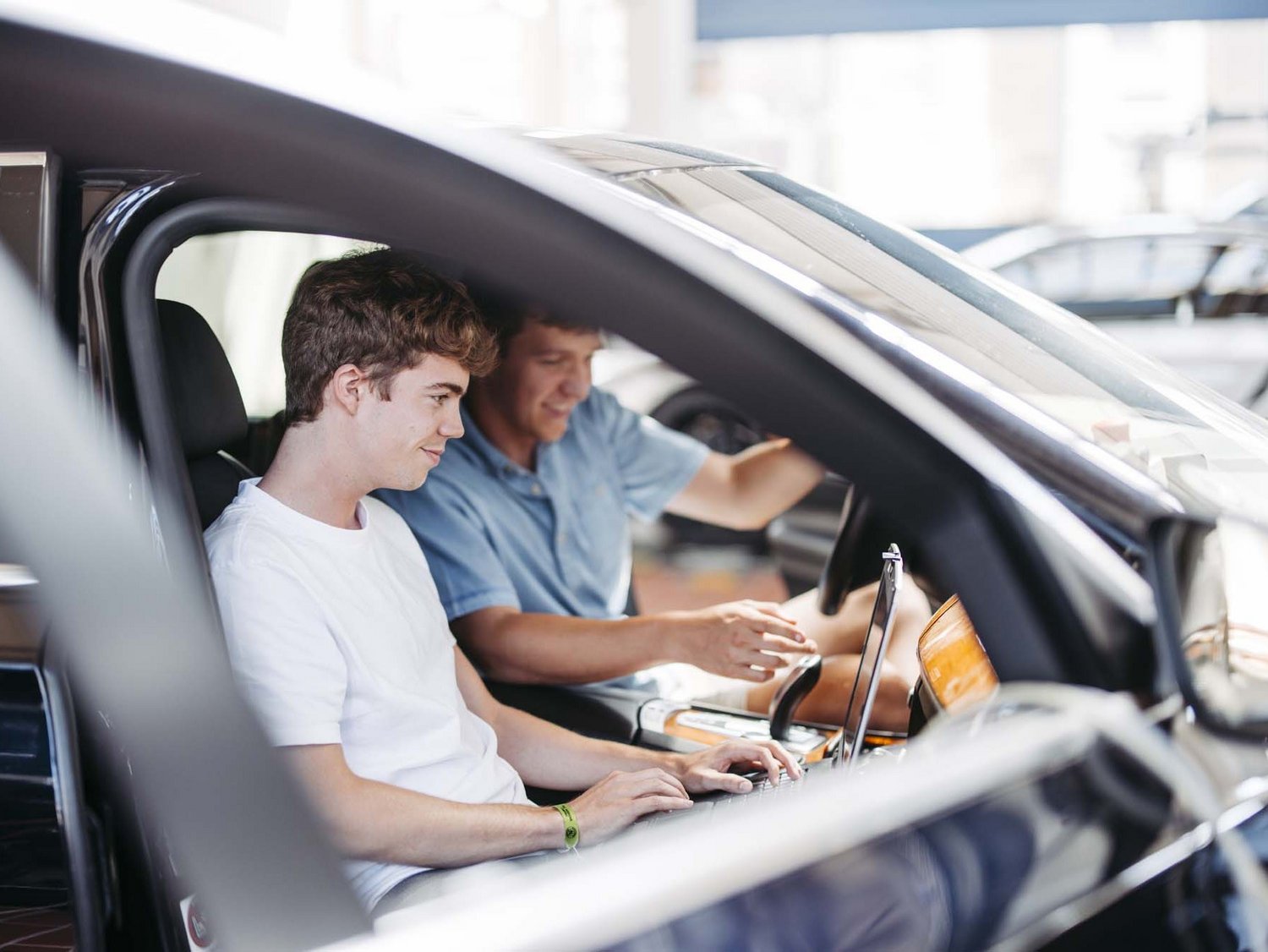 Zwei Personen sitzen in einem Fahrzeug die eine hat ein Laptop auf ihrem Schoß die andere Person schaut in den Laptop mit rein.