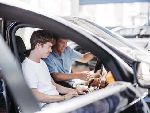 Zwei Personen sitzen in einem Fahrzeug die eine hat ein Laptop auf ihrem Schoß die andere Person schaut in den Laptop mit rein.