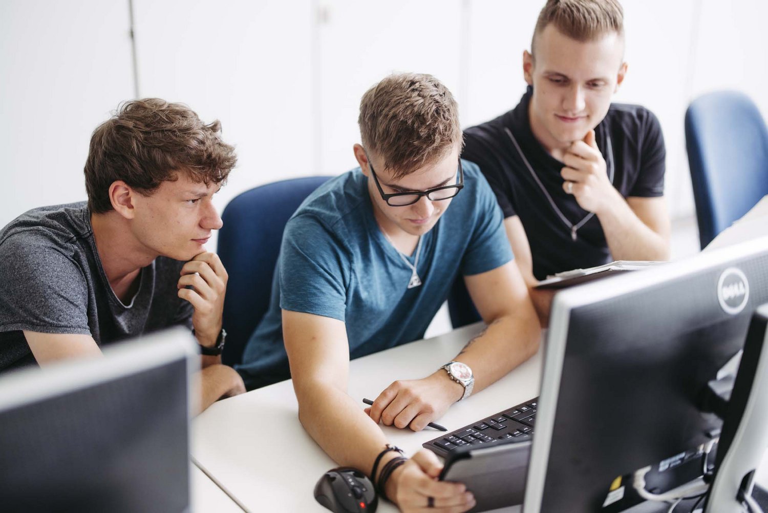 Drei Personen sitzen nebeneinander in einem Raum und schauen auf den vor ihnen stehenden Computer.