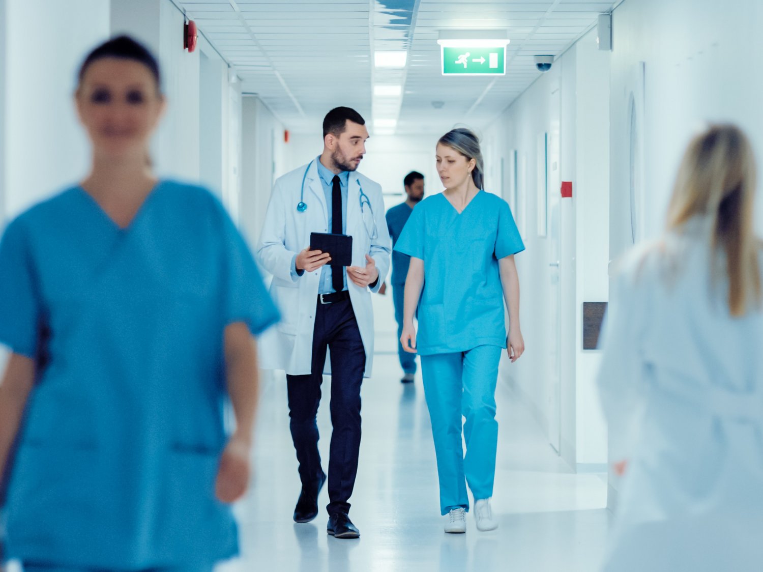 In einem Klinikflur gehen mehrere personen. Zwei Personen reden miteinander.