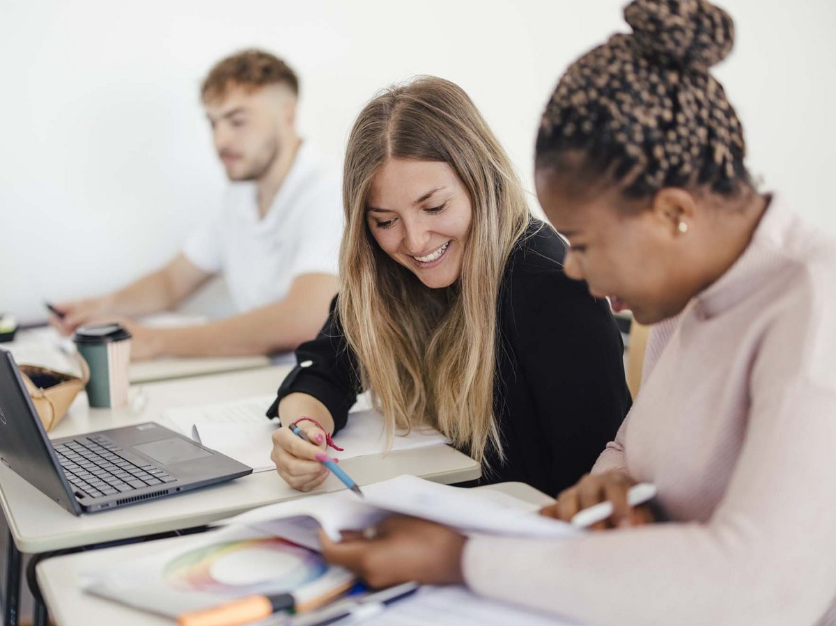 Zwei Personen sitzen zusammen und lernen. Eine Person sitzt dahinter und lernt alleine am Computer.