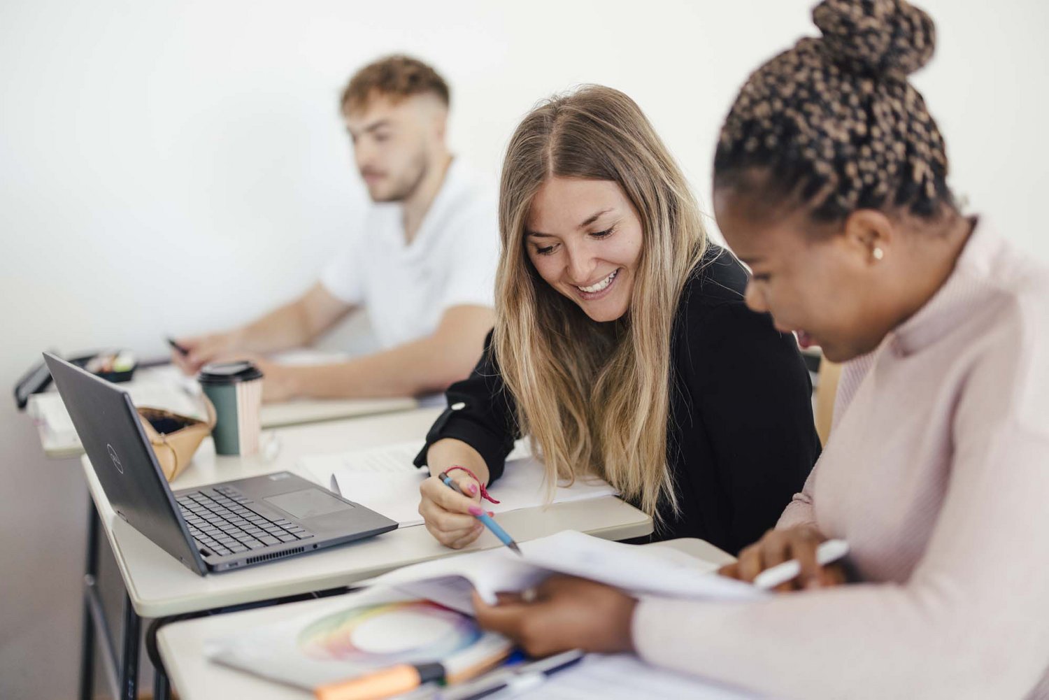 Zwei Personen sitzen zusammen und lernen. Eine Person sitzt dahinter und lernt alleine am Computer.