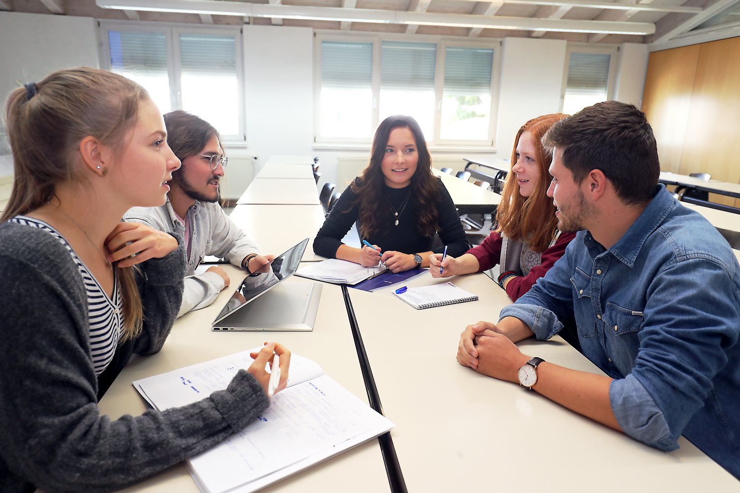 Fünf Studierende sitzen gemeinsam an einem Tisch und lernen zusammen.