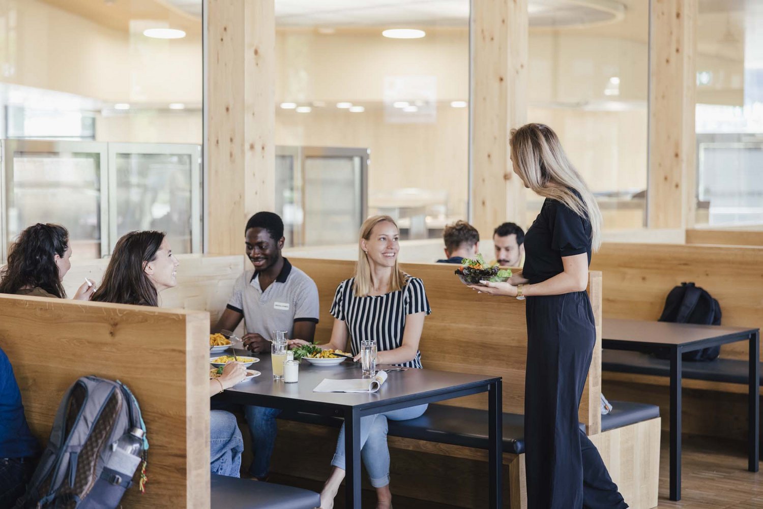 Man sieht vier Personen an einem Tisch sitzen und eine Person steht davor, alle haben was zu essen.