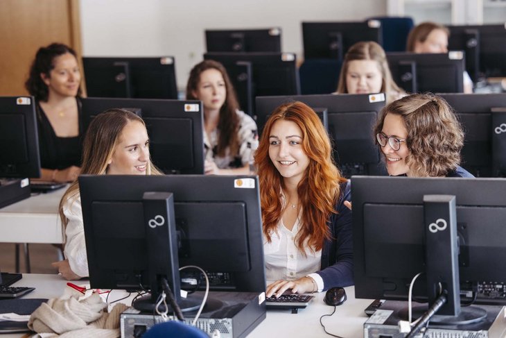 Drei Personen sitzen nebeneinander und schauen in einen Computer rein.