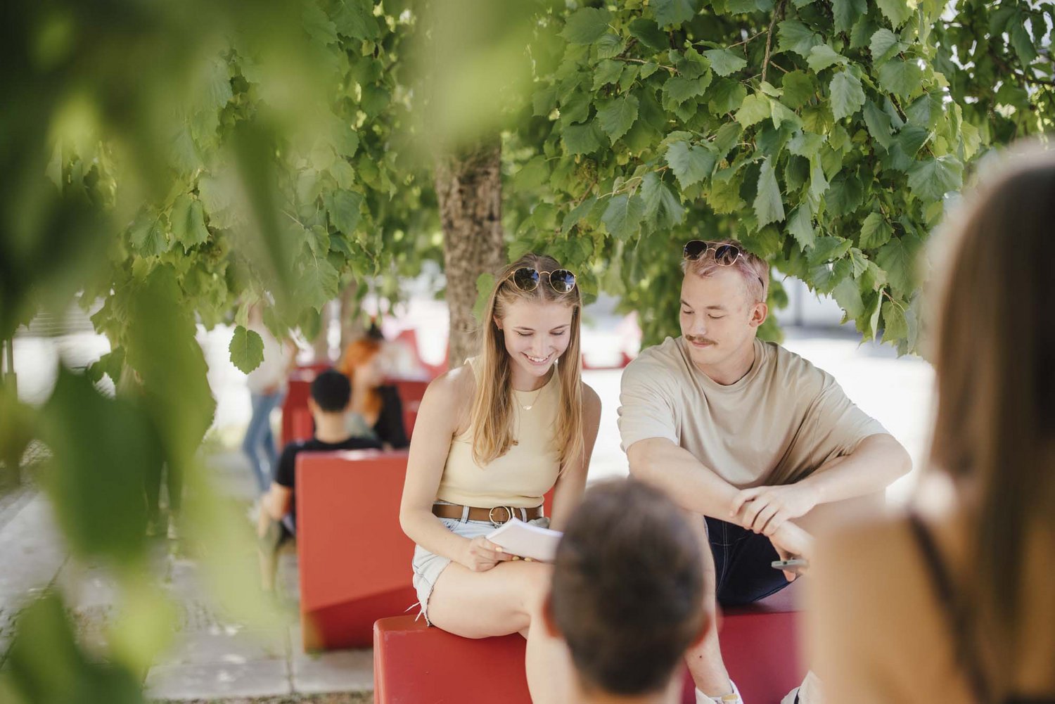 Studierende sitzen draußen an einem Enzo und unterhalten sich