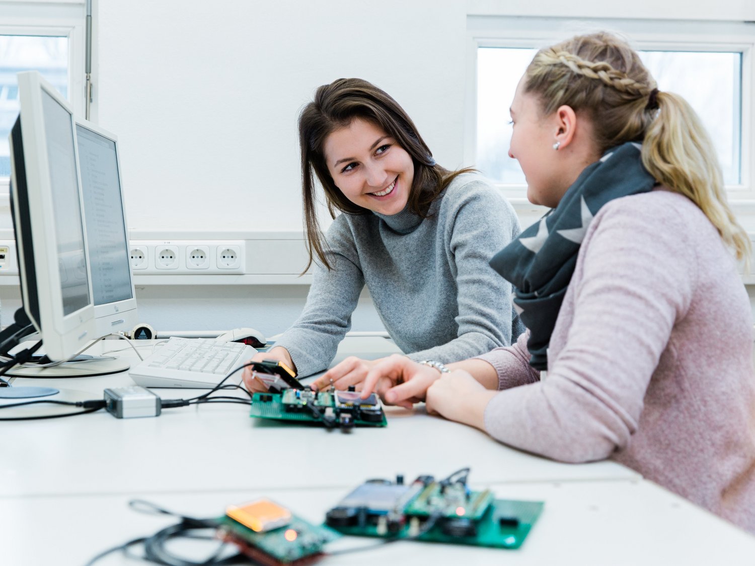 Zwei Studierende sitzen an einem PC-Arbeitsplatz mit Entwicklungsboards für die Programmierung von Mikrocomputern.