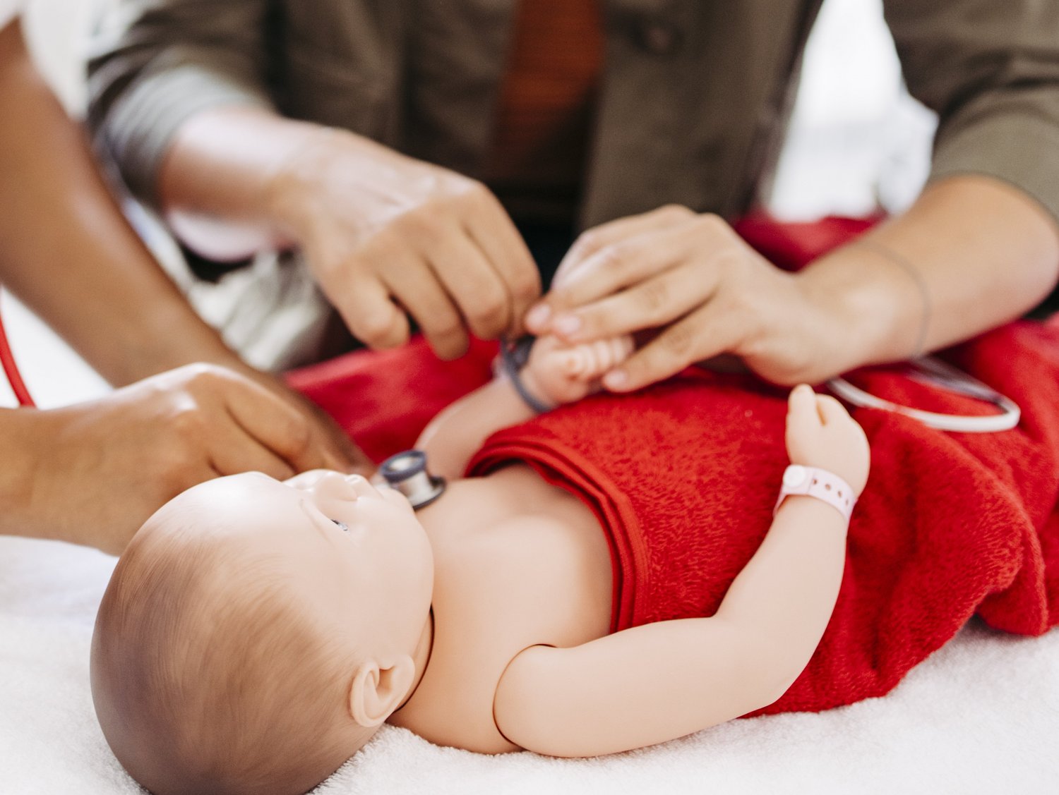 Eine Frau hört eine Babypuppe ab, welche in einer Neugeborenen-Reanimationseinheit liegt. Eine weitere Frau legt der Puppe einen Sensor an.