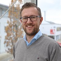 Eine Person steht vor einer Glaswand und lächelt.