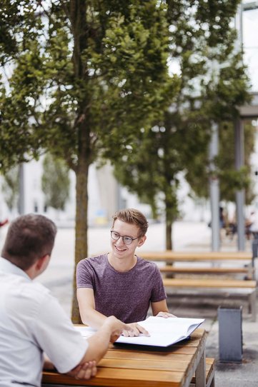 Zwei Personen sitzen draußen an einem Tisch. 