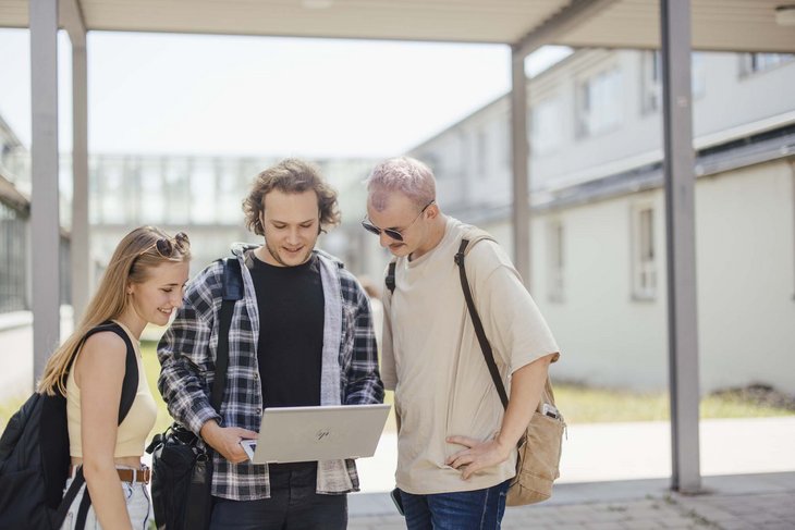 Studierende stehen draußen und schauen auf einen Laptop