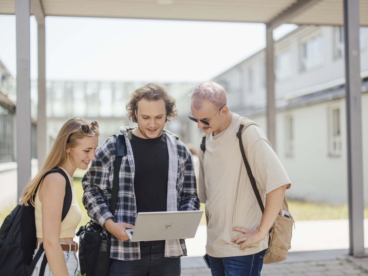 Studierende stehen draußen und schauen auf einen Laptop