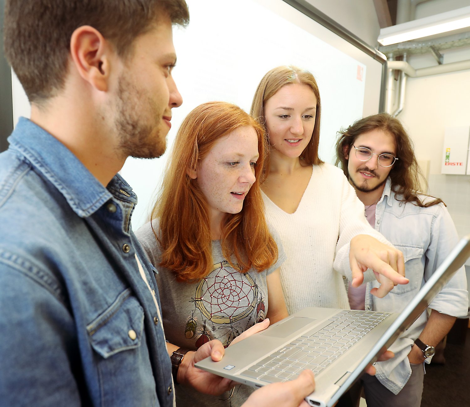 Vier Studierende schauen gemeinsam auf den Bildschirm eines Laptops. 