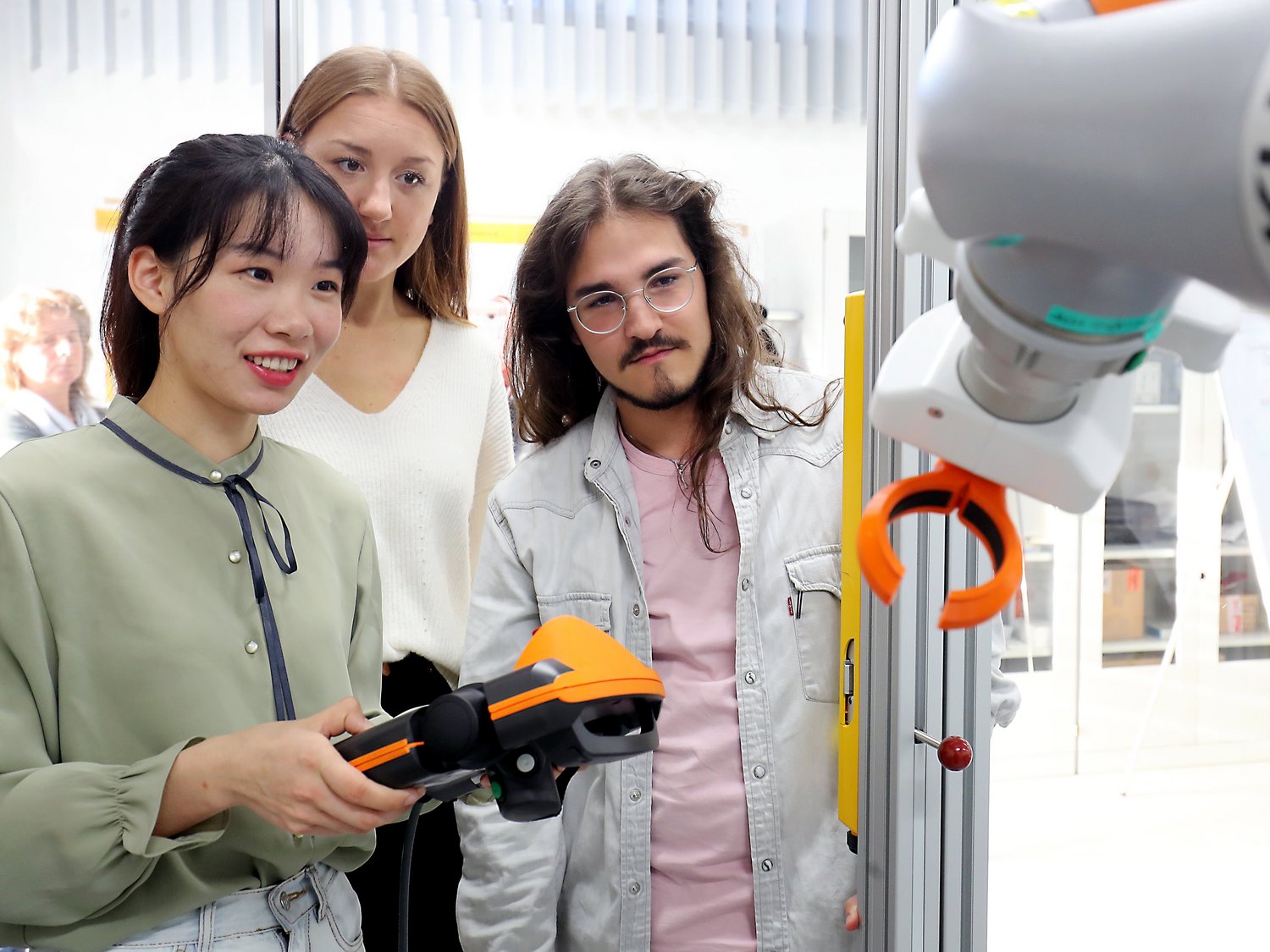 Drei Personen stehen vor dem Arm eines Roboters. Eine Person hat ein Bedienfeld in der Hand.