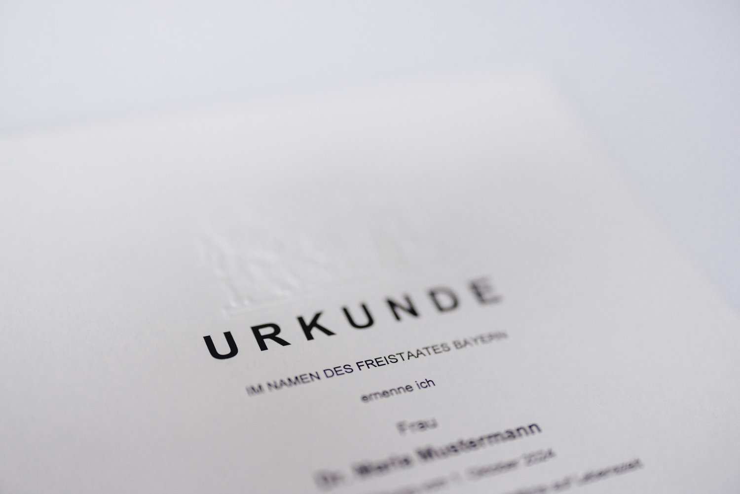 Ein Dokument mit dem Titel "URKUNDE" in Großbuchstaben, das im Namen des Freistaates Bayern ausgestellt ist. Es enthält eine Prägung und ist auf weißem Papier gedruckt. Der Text ist teilweise unscharf.