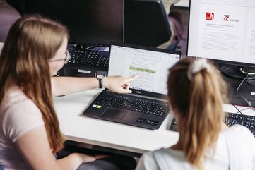 Zwei Personen sitzen nebeneinander und schauen in einen Computer hinein.