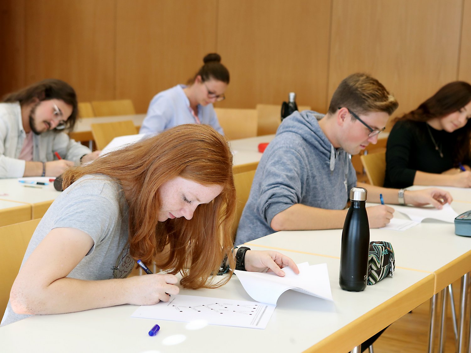 Fünf Personen sitzen in einem Vorlesungsraum und schreiben auf Blättern.