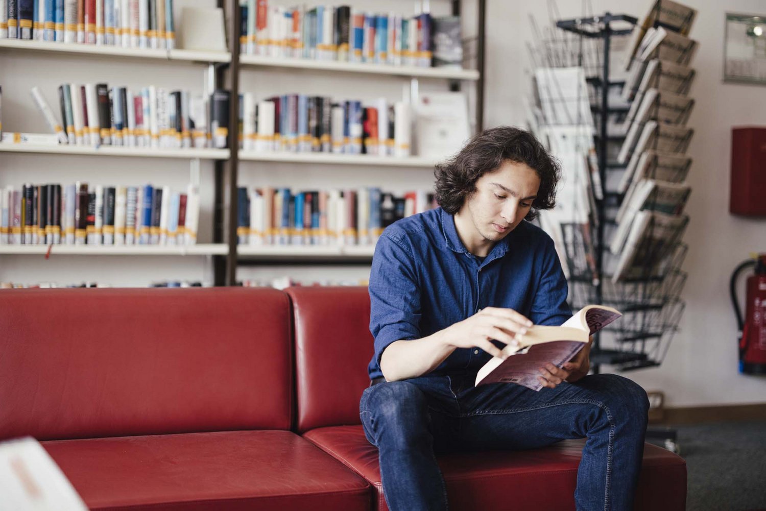 Eine Person sitzt auf einer Couch und liest ein Buch.