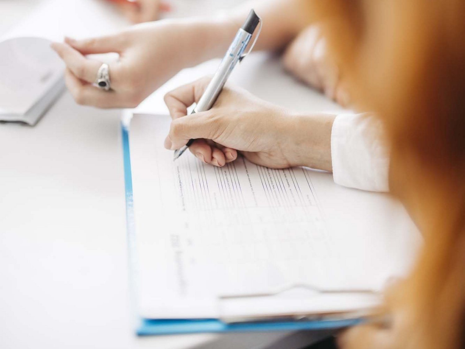 Auf einem Tisch liegt ein Blatt und man sieht eine Hand die einen Stift hält.