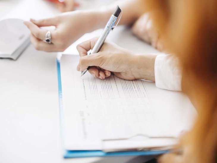 Auf einem Tisch liegt ein Blatt und man sieht eine Hand die einen Stift hält.