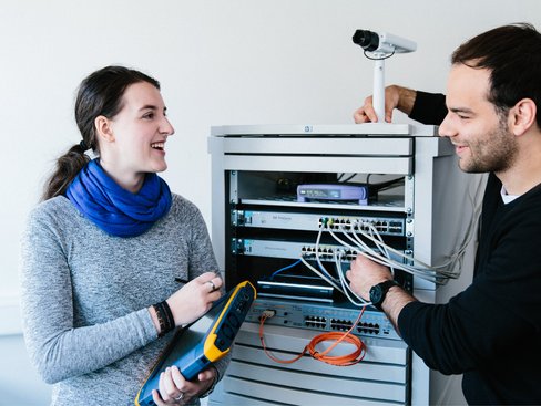 Zwei Studierende untersuchen einen Aufbau mit Netzwerkkomponenten.