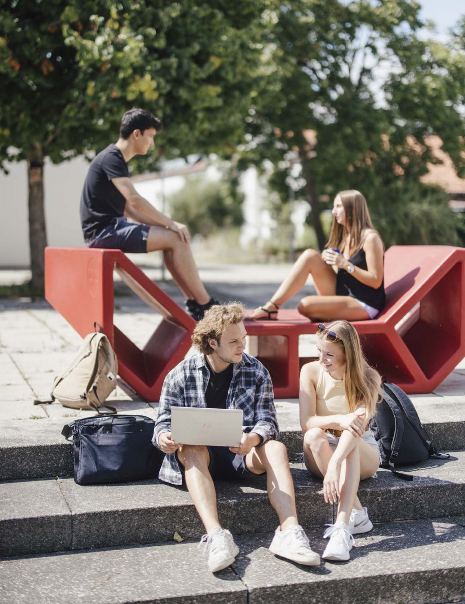 Studierende sitzen draußen an einem Enzo und unterhalten sich