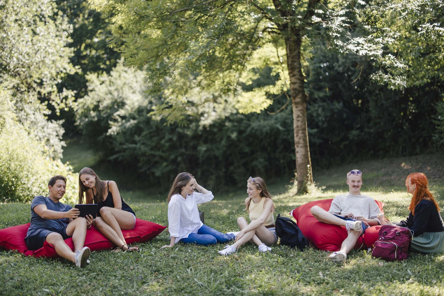 Studierende sitzen mit Sitzkissen im freien unter Bäumen