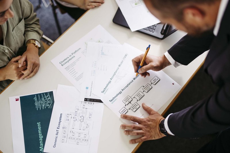 Eine Person steht vor einem Tisch. Auf dem Tisch liegen Blätter verteilt.