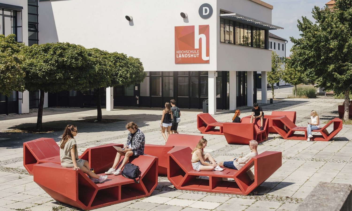 Blick auf das D-Gebäude mit Studierenden sitzend auf den Enzos