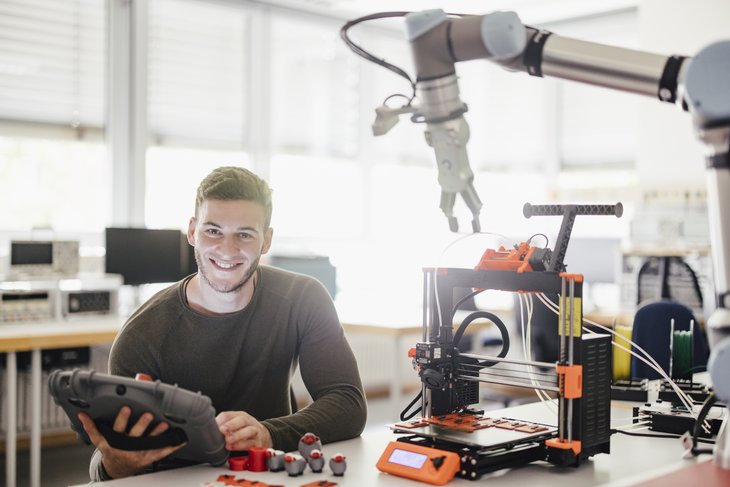 Ein Studierender an einem Arbeitsplatz mit Cobot und 3D-Drucker