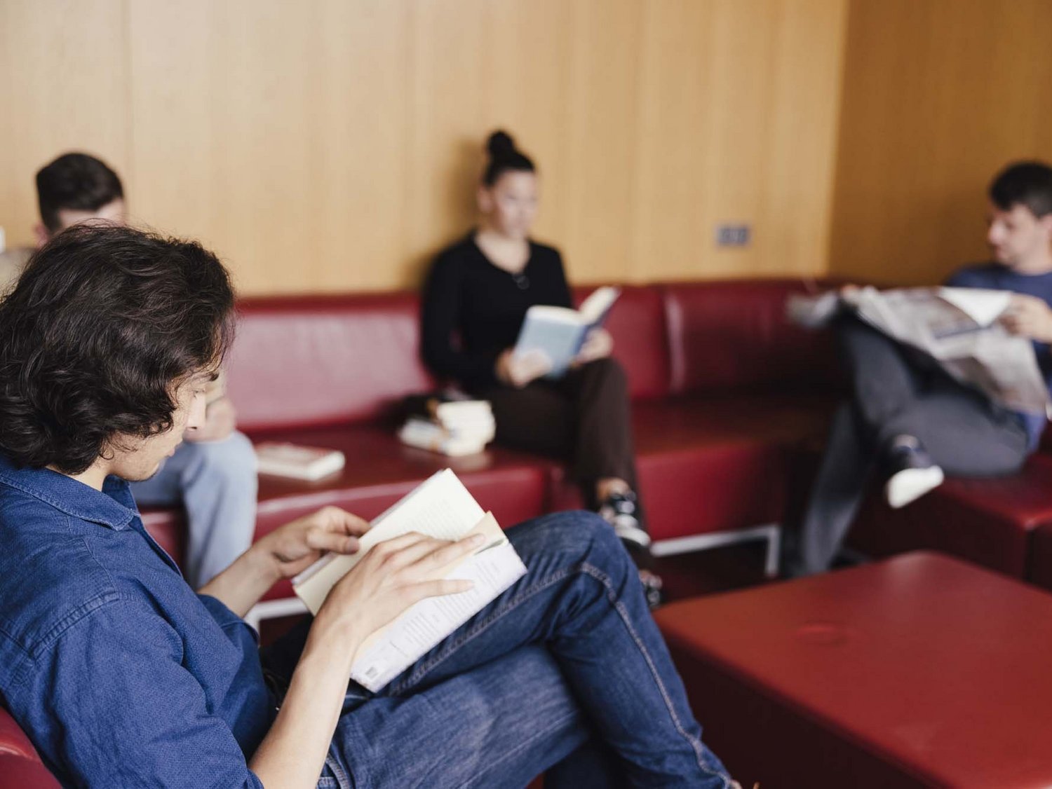 Eine Person sitzt auf einer Couch und liest ein Buch.