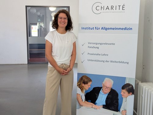 Prof. Dr. Katrin Liel steht vor einem Werbeaufsteller der Charité Berlin