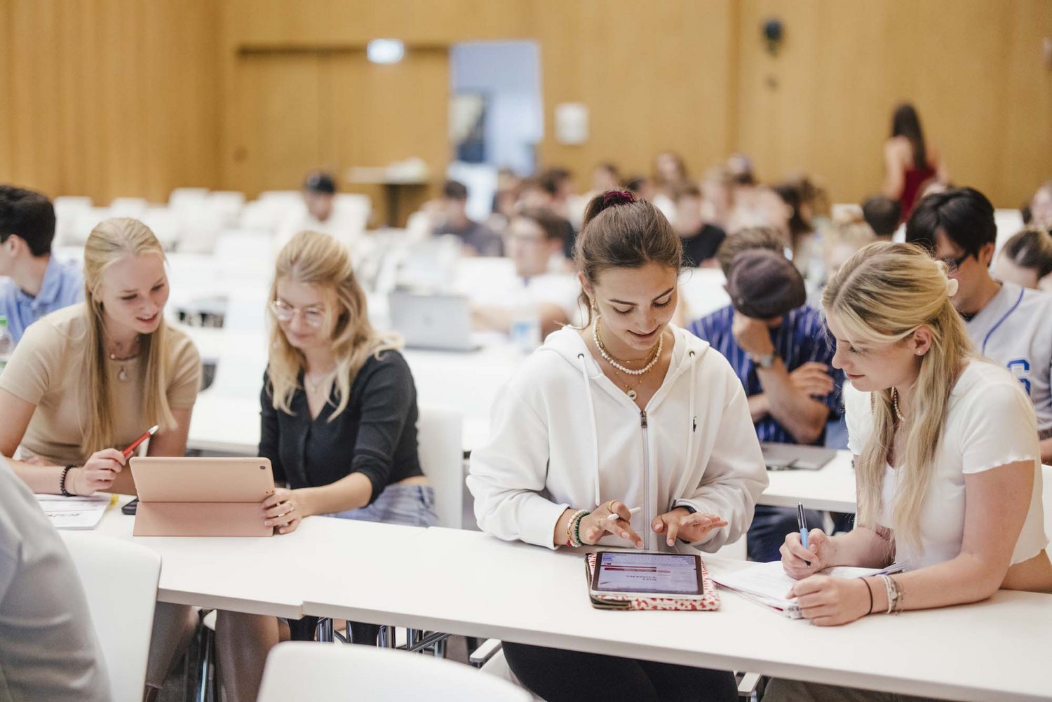 Vier Personen sitzen in einer Reihe in einem Lehrsaal , jeweils zwei von ihnen schauen zusammen in ein Tablet hinein.