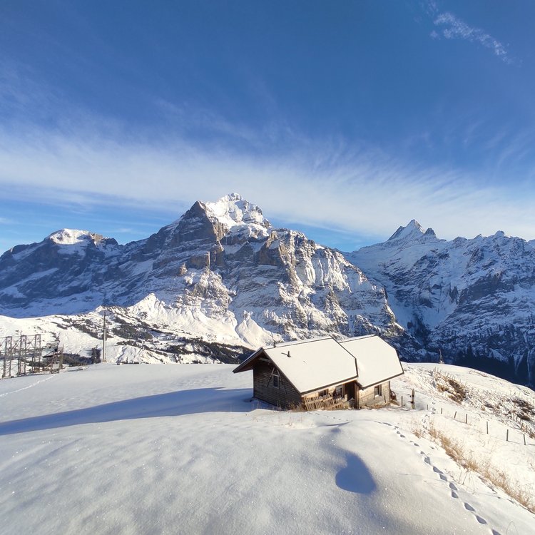 Eine Holzhütte auf verschneiten Gipfeln eines Bergpanoramas.