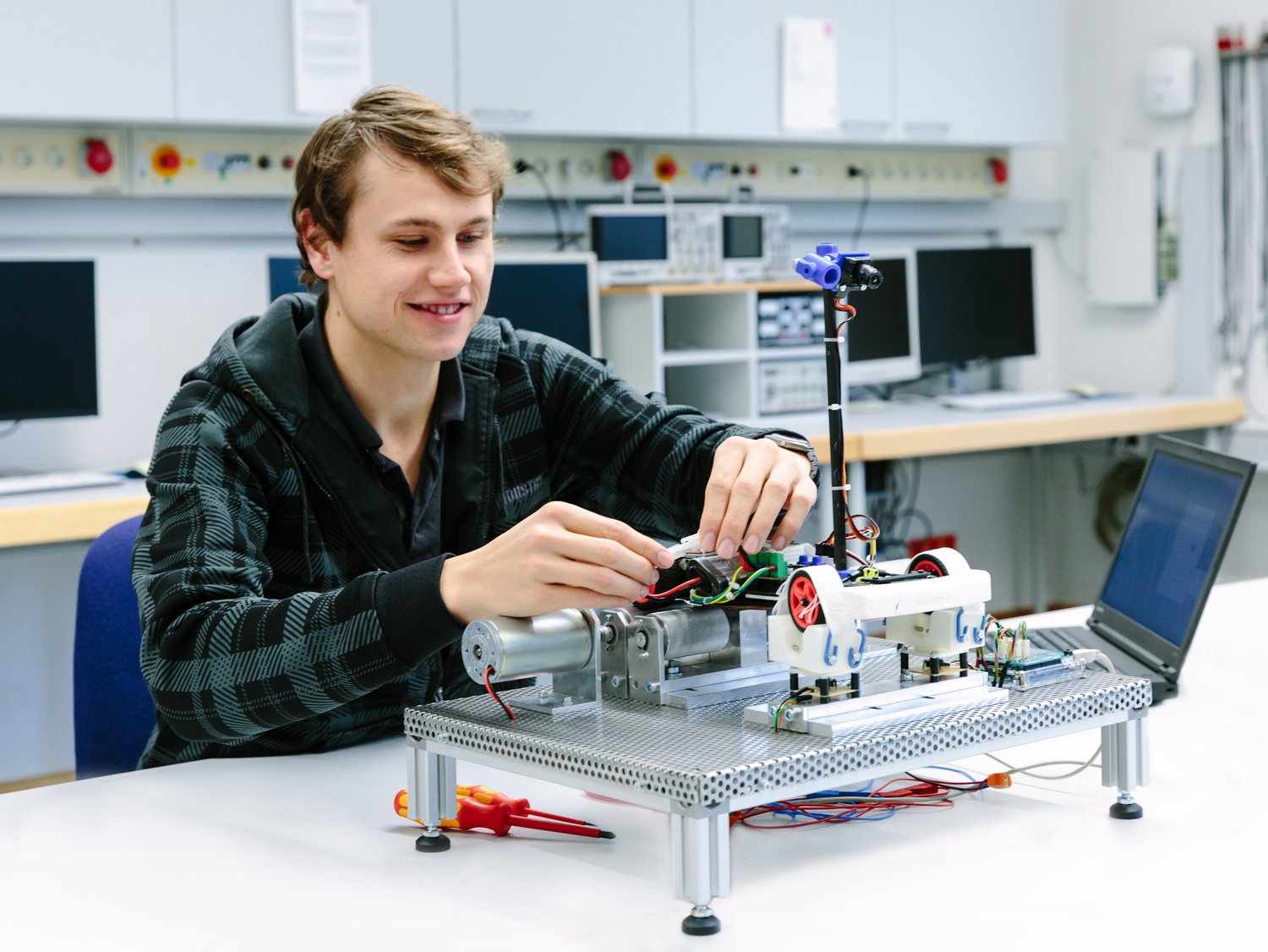 Ein Studierender nimmt ein kleines autonomes Fahrzeug auf einem Teststand in Betrieb.