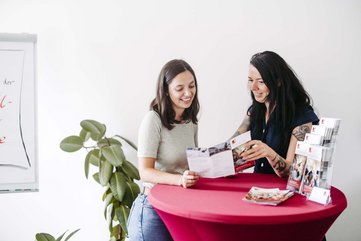 Zwei Personen stehen nebeneinander und schauen zusammen in ein Dokument.