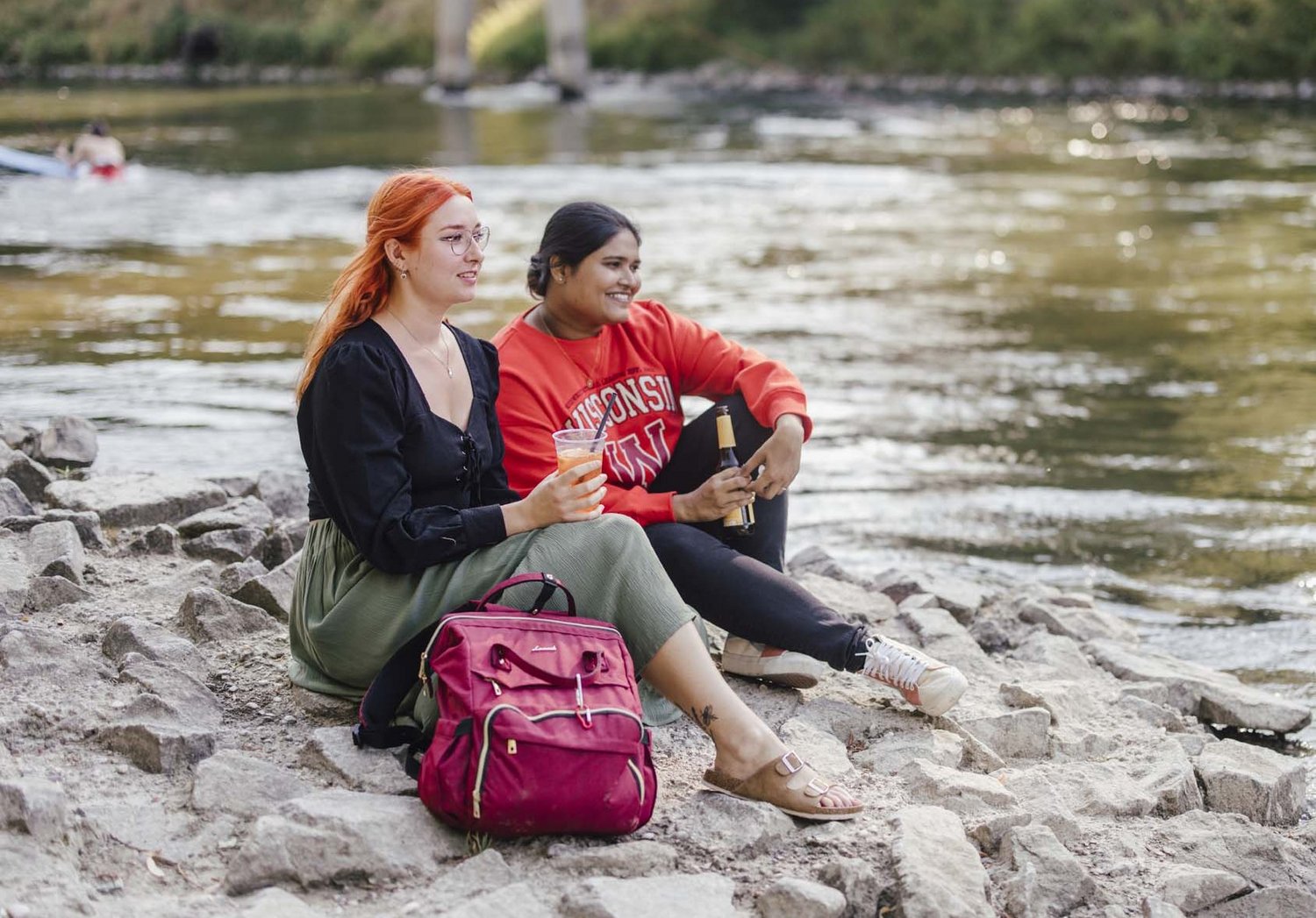 Zwei Personen sitzen am Wasser mit Ihren Getränken