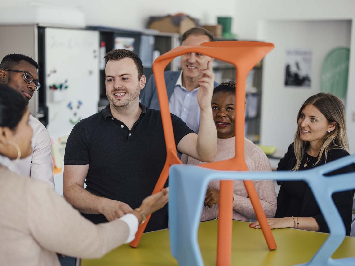 Eine Gruppe steht um einen Tisch herum, auf welchem Figuren positioniert worden sind. Einer der Personen erklärt, die restlichen Personen hören zu.